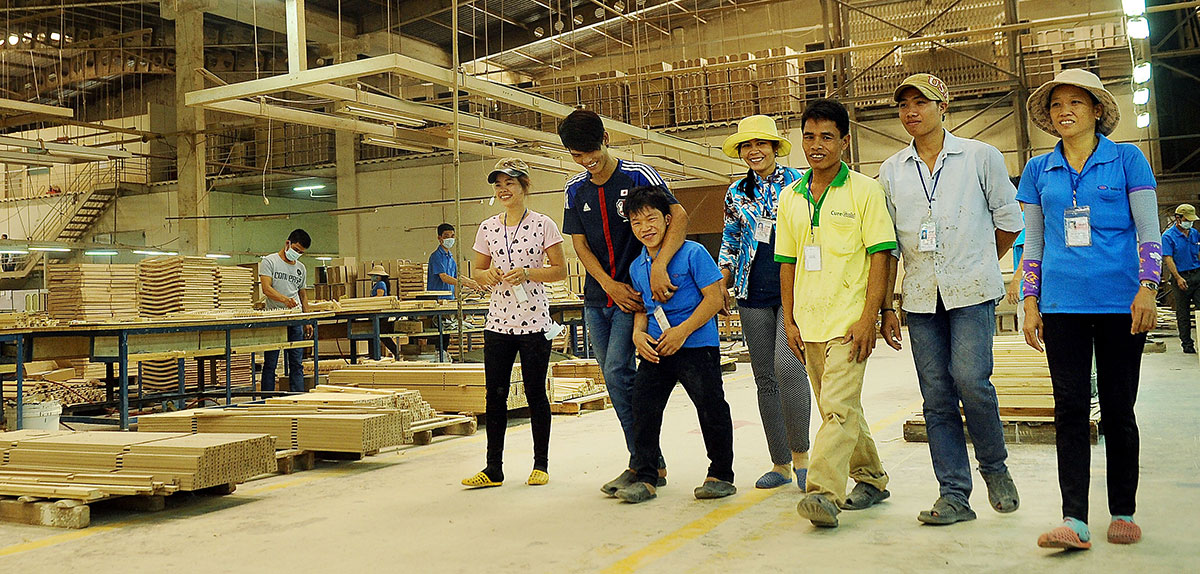 Group of workers with and without disability walking through wood mill with others working in the background