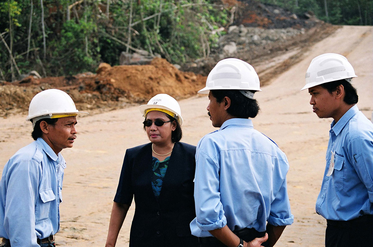 Three men and one woman with hard hats talking on dirt road