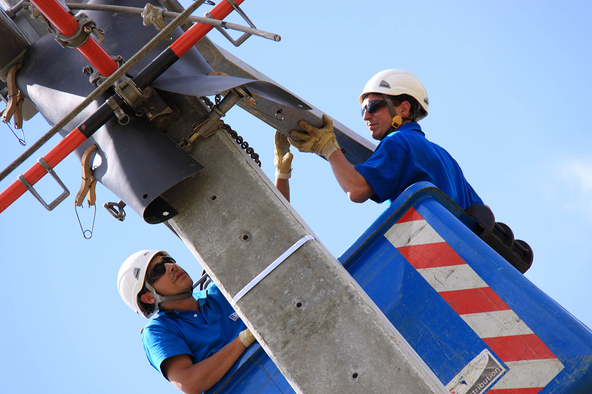 Two men at the top of a pole working on a power line