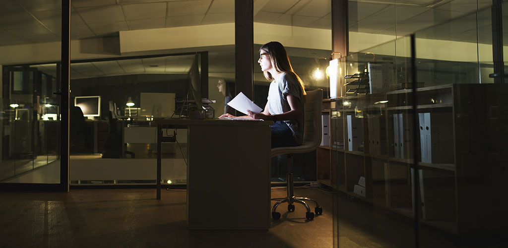 Lady working on laptop at desk at night in empty office