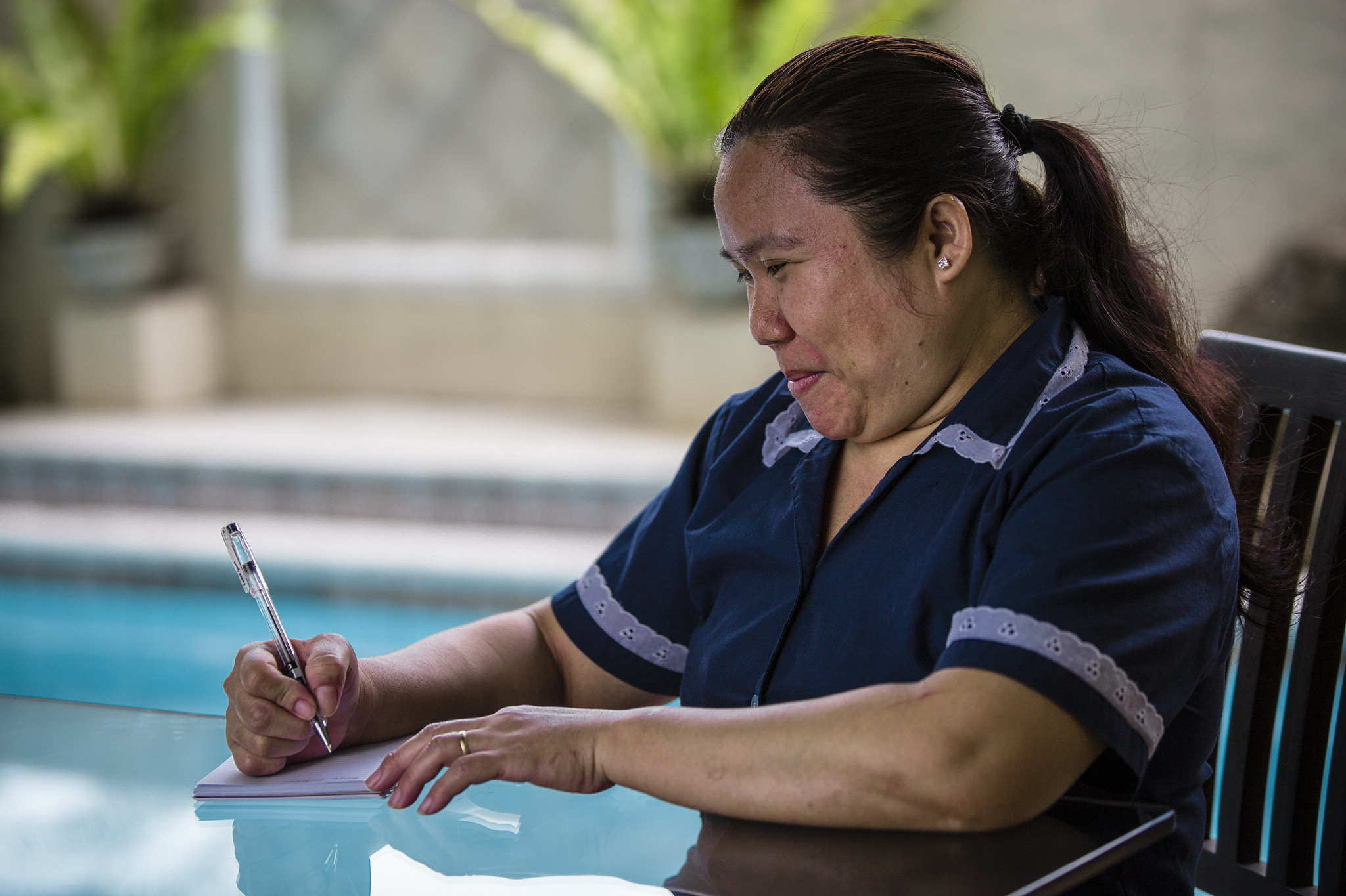  Domestic Workers in the Philippines writing in pad on table by pool