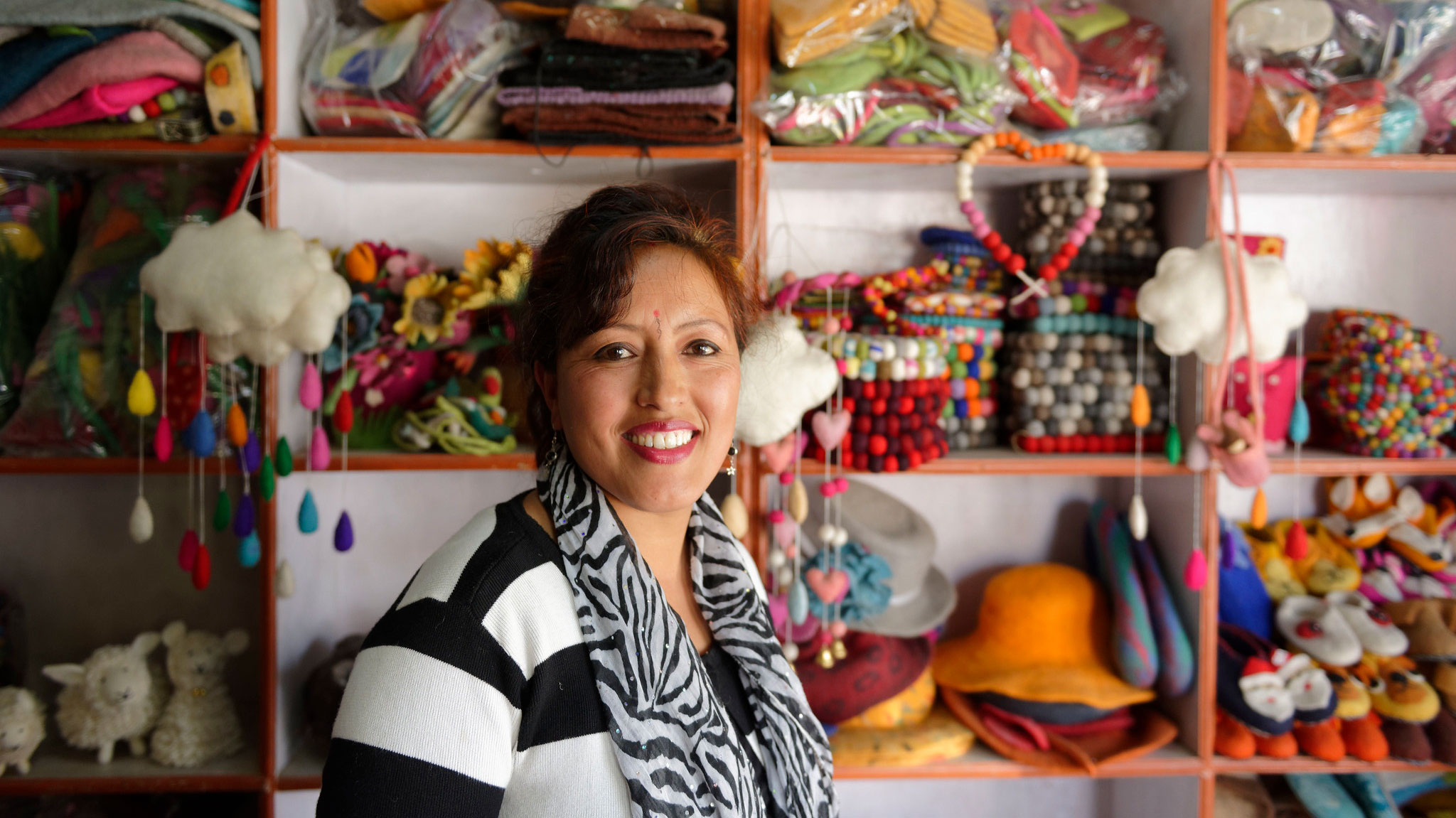 Lady owner of shop in Nepal with shelves of colourful handcrafted items 