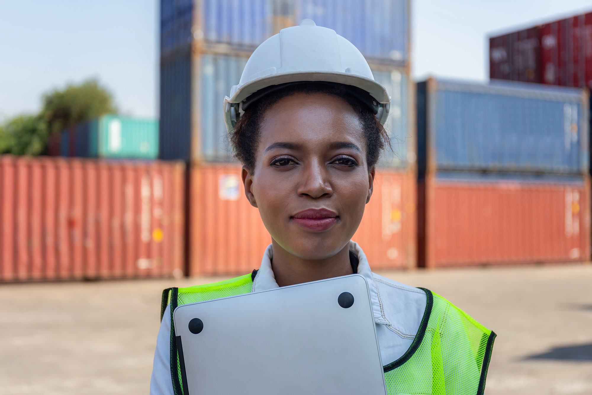 Young lady with hard hat and clip board with containers behind her