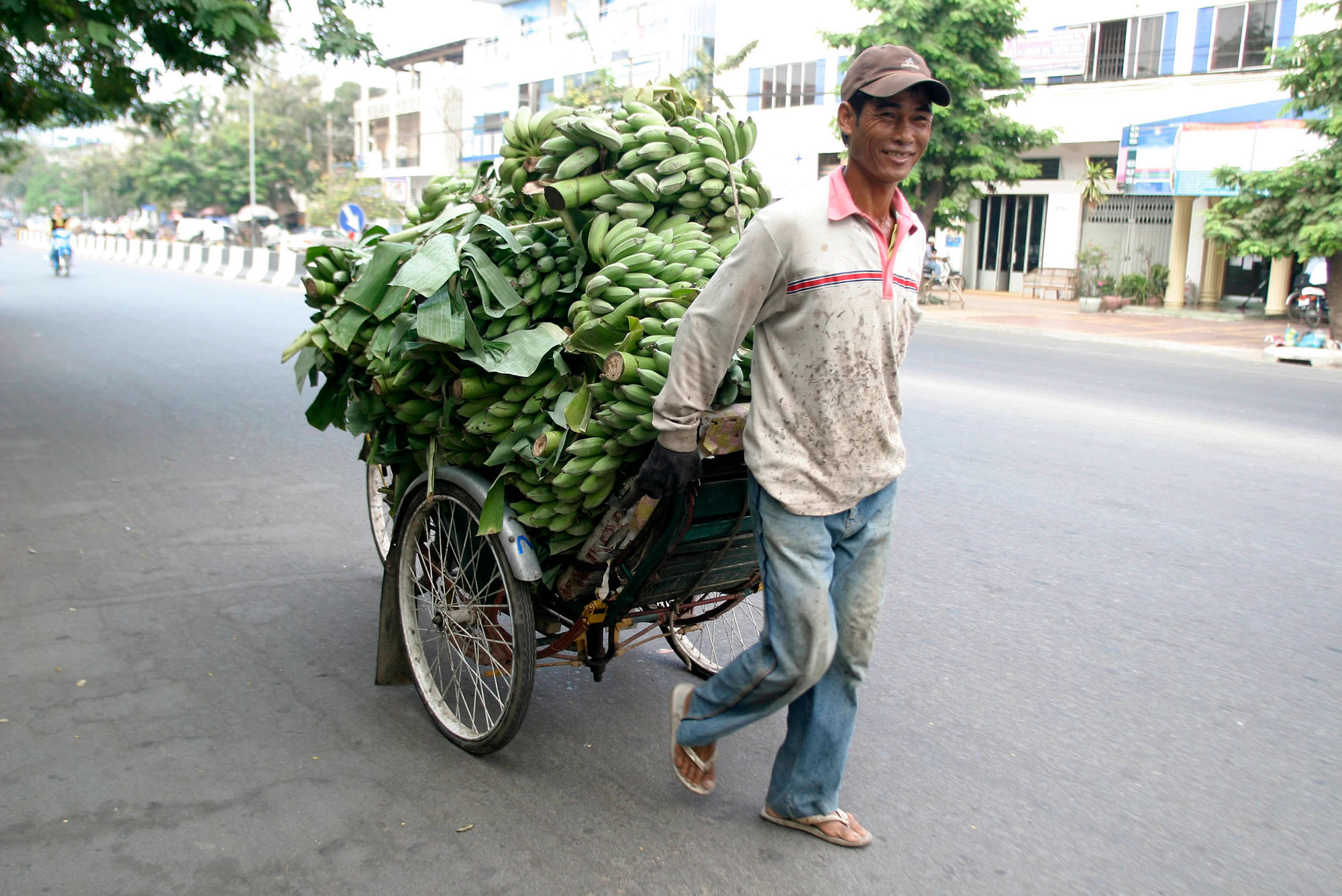 Young man pulling cart full of green bananas on empty street in Cambodia