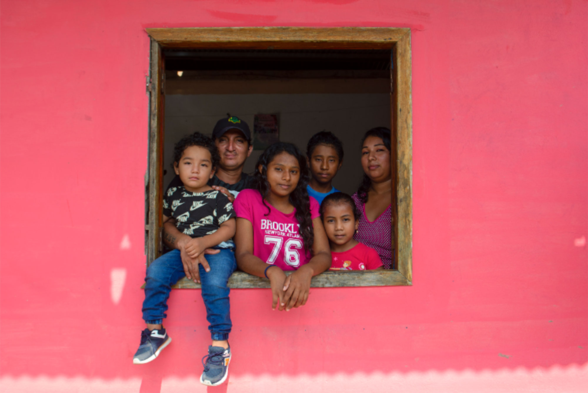 Family group looking through a window surrounded by pink wall