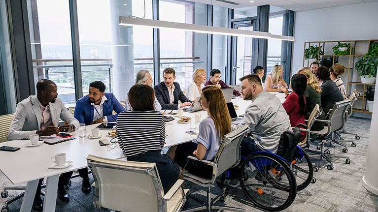 Group of work colleagues, one with wheelchair, talking around a conference table