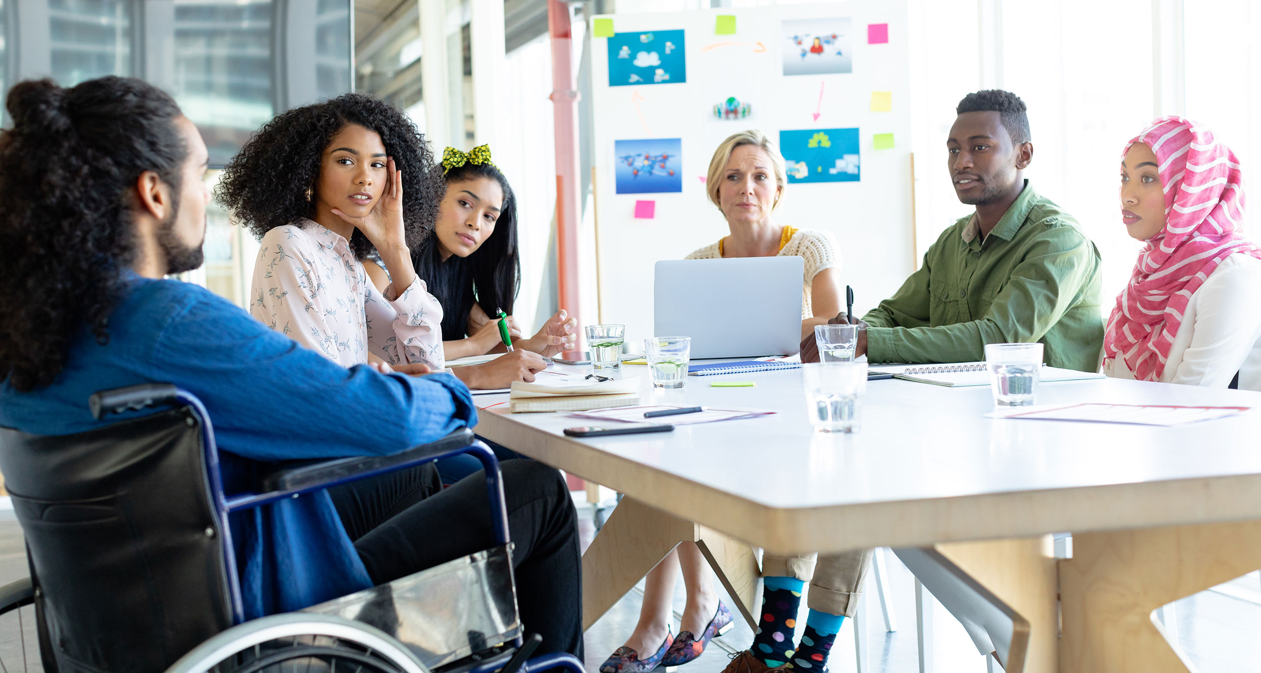 Group of ethnic diverse workers in office space smiling around desk, one in wheelchair