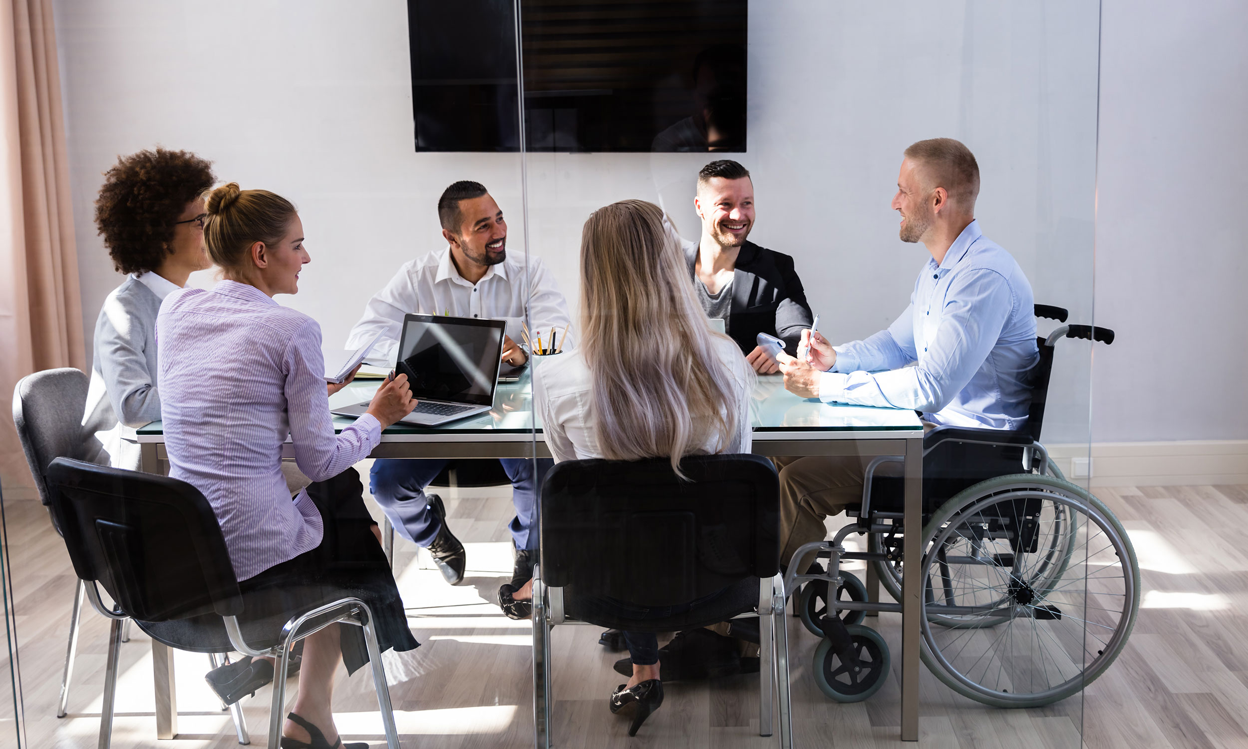 Group of work colleagues, one with wheelchair, talking around a conference table