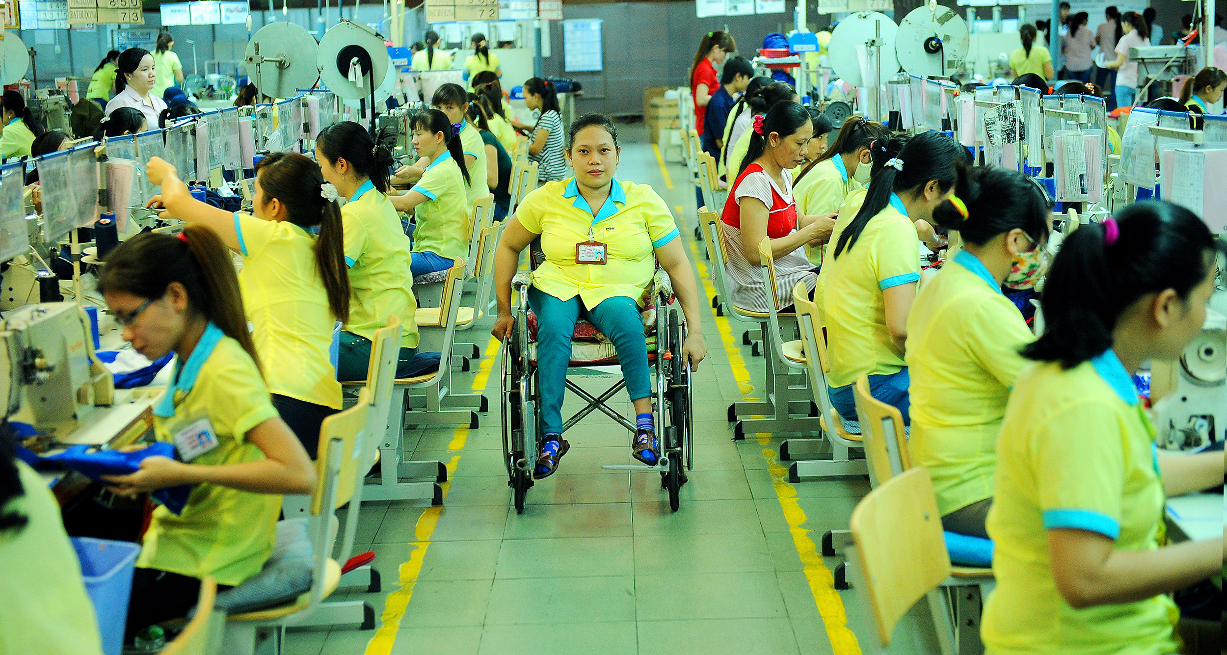 Factory workers in yellow uniform working with sewing machines with one worker in a wheelchair