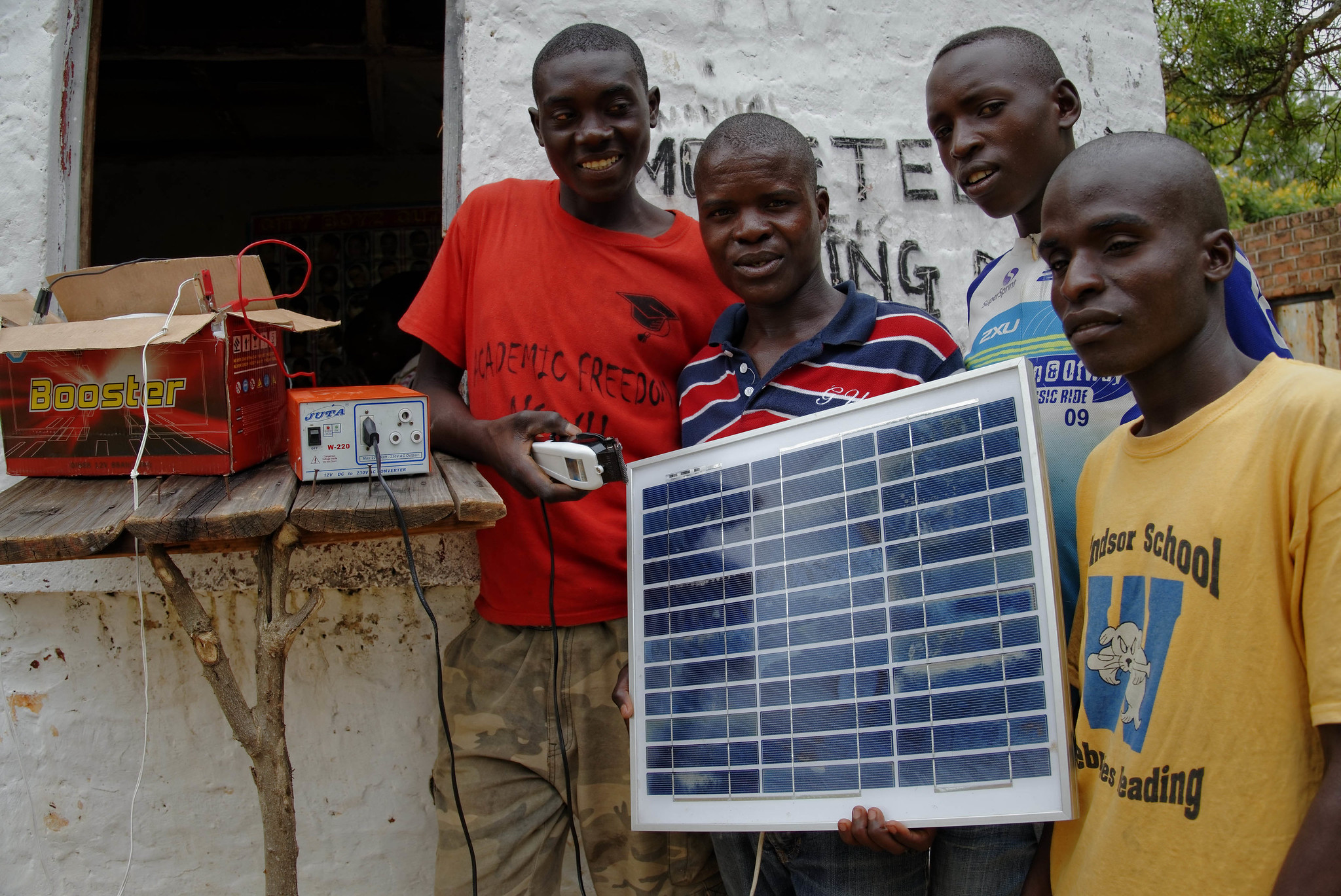 Group of 4 young black men smiling and holding a small solar panel with a portable battery charger