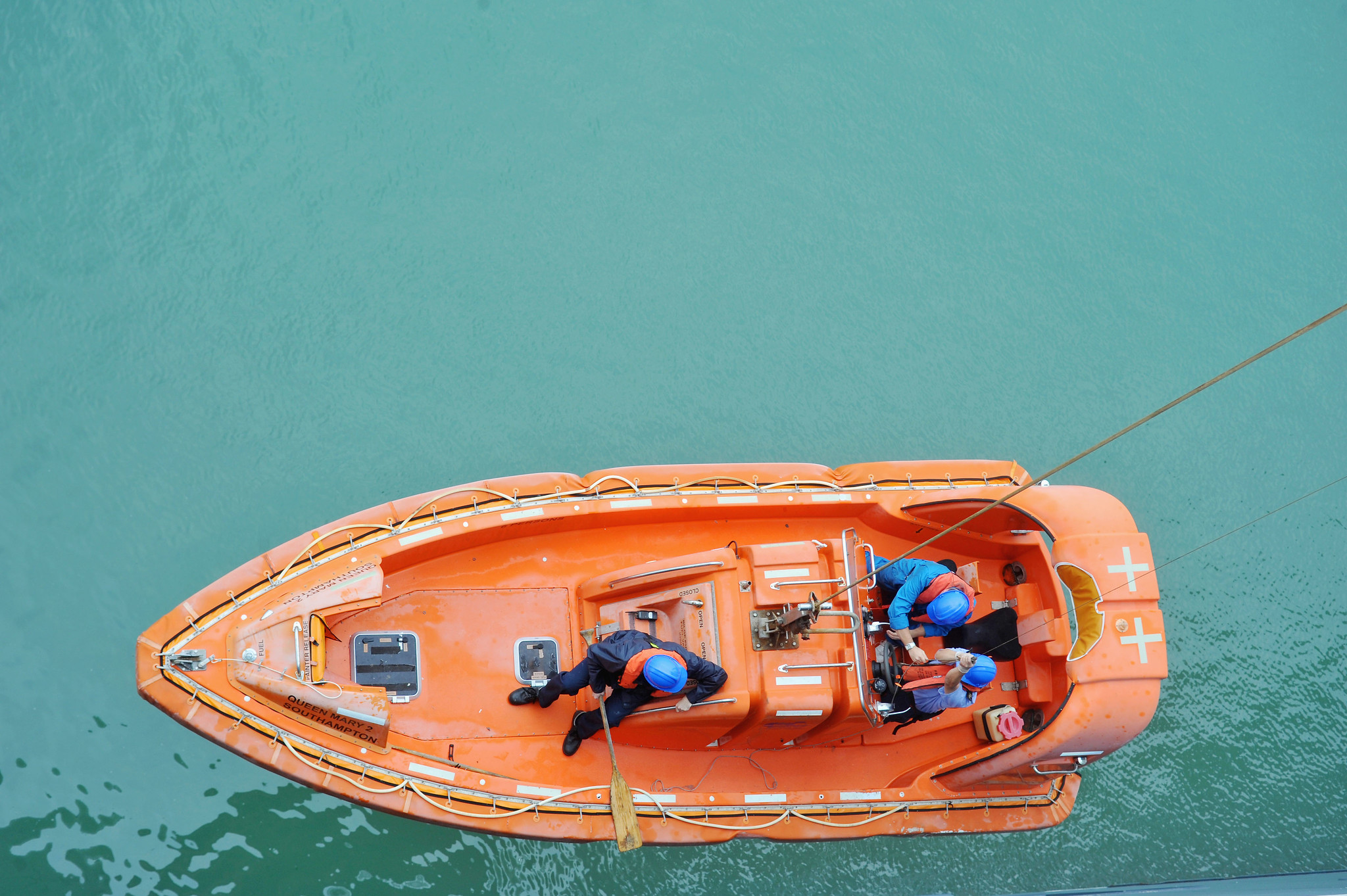 Arial view of an organe lifeboat with 3 people being hauled above the sea
