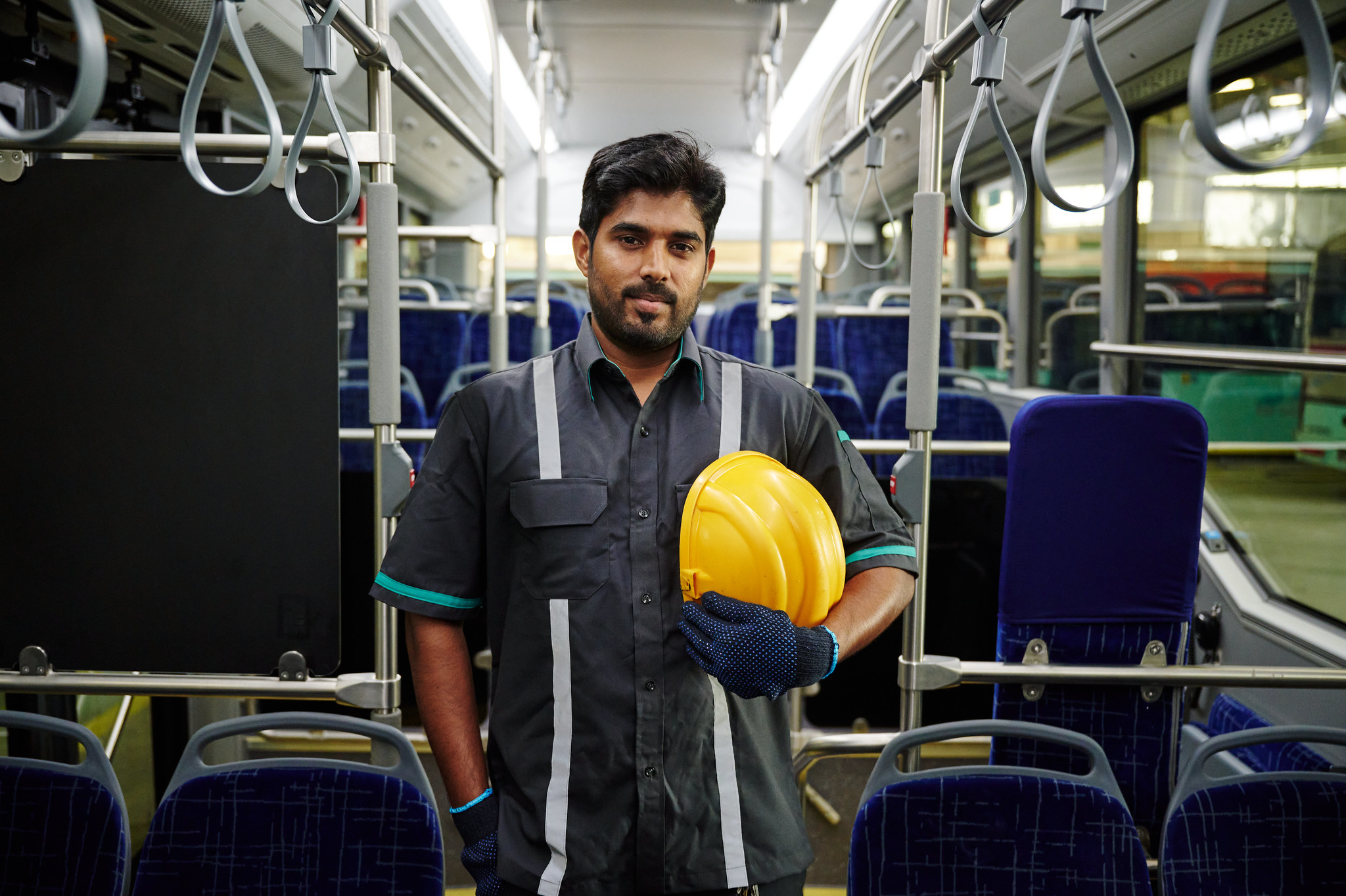 Young  Indian man with standing in an empty train holding yellow hard hat in left hand 