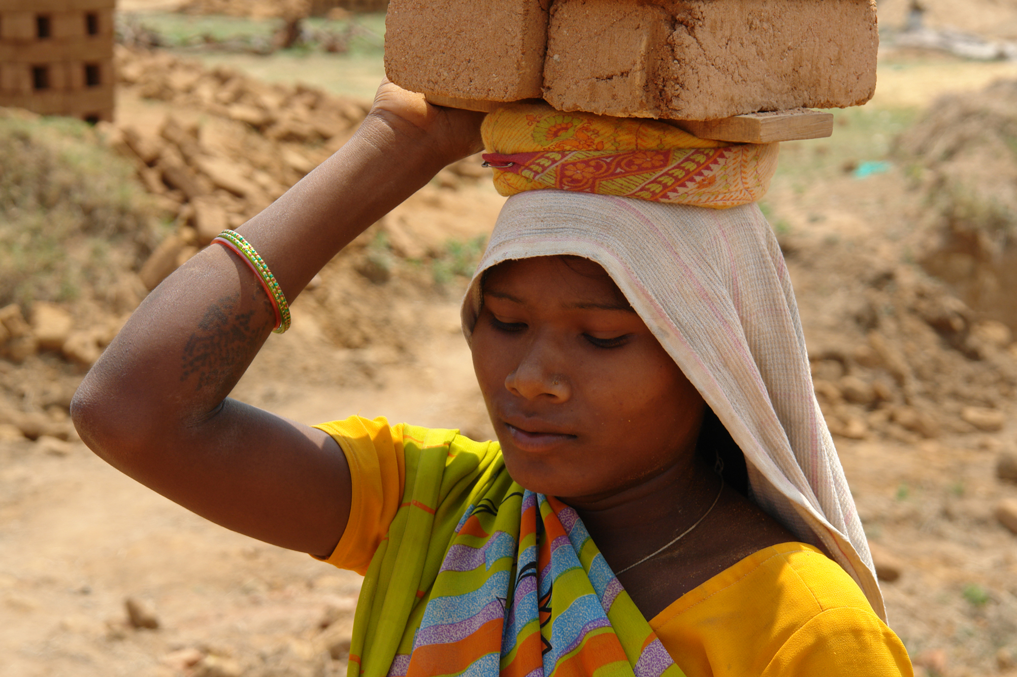 Young lady with yellow sari carrying woven basket on her head