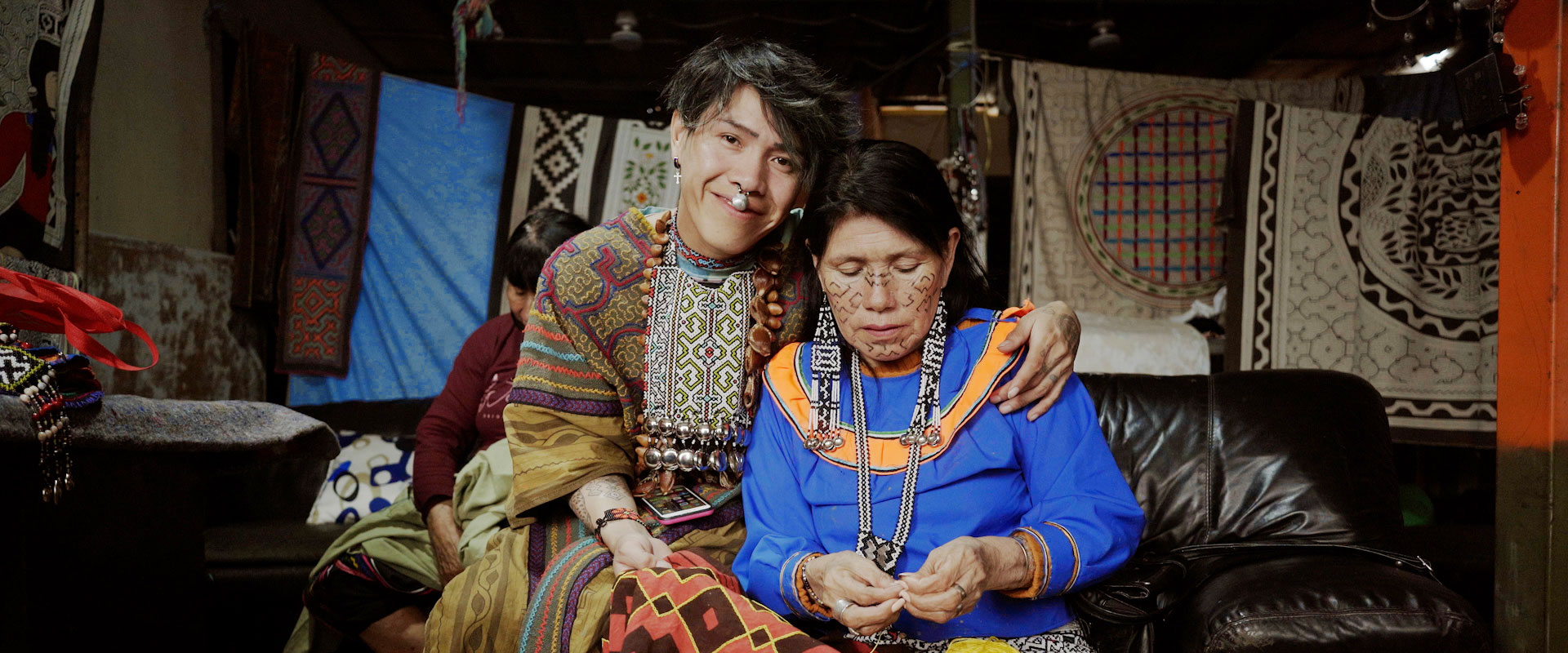 Young man with peircing with arm around woman sewing, both in traditional dress