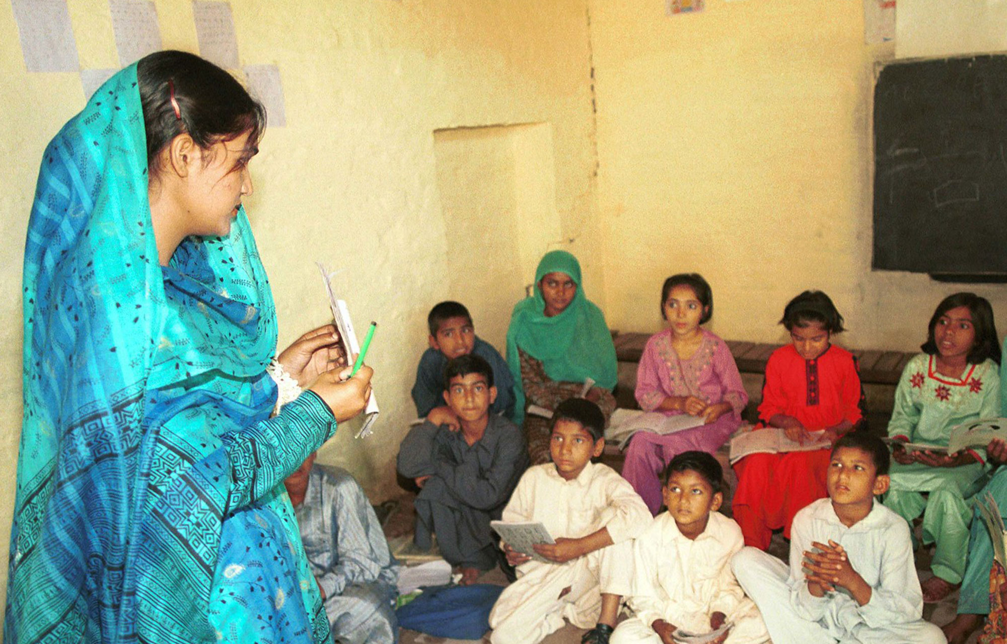 Lady in turquoise sari teaching group of children sat on the floor in Pakistan 