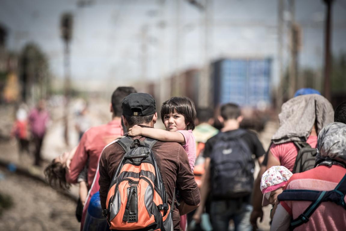 A man walks with a group, carrying a kid in his arms © S.Ryan-IFRC