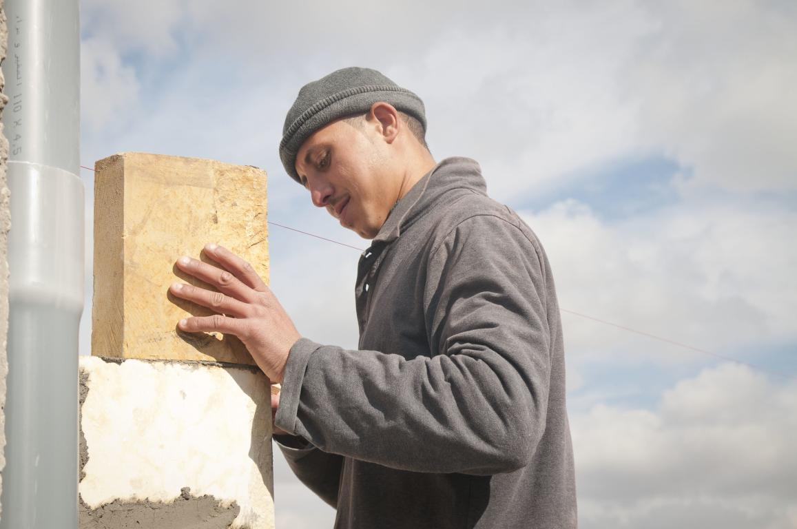 Man in grey jumper and wool hat laying a breeze block 