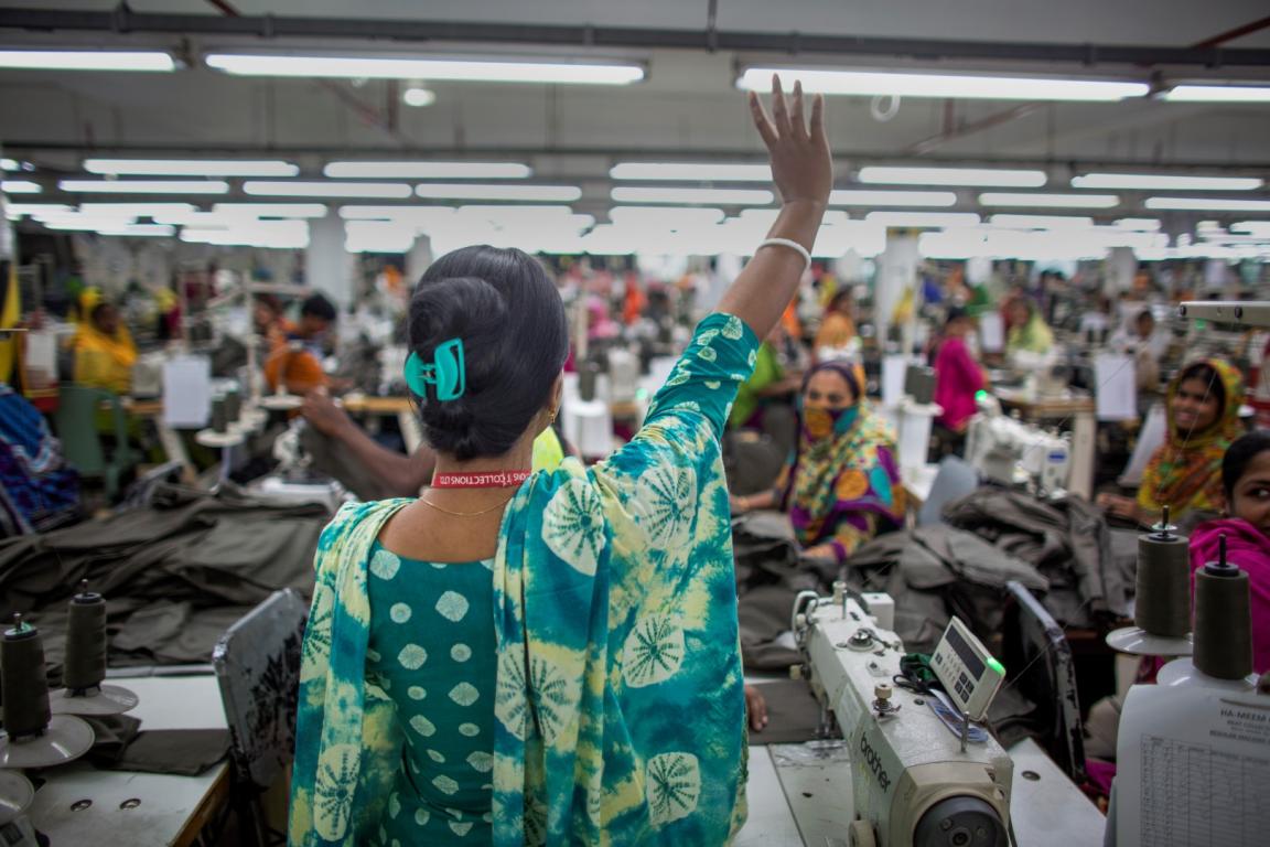 Bangladeshi woman worker, stands in a garment factory, raising her hand, facing her fellow co-workers