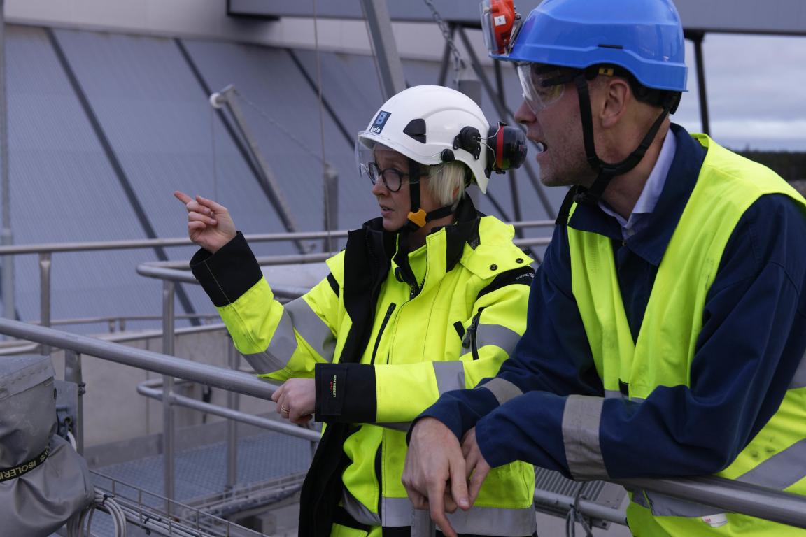 Man and women with hard hats and reflective vests looking to left on metal construction