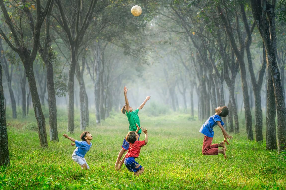 four boy playing ball on green grass