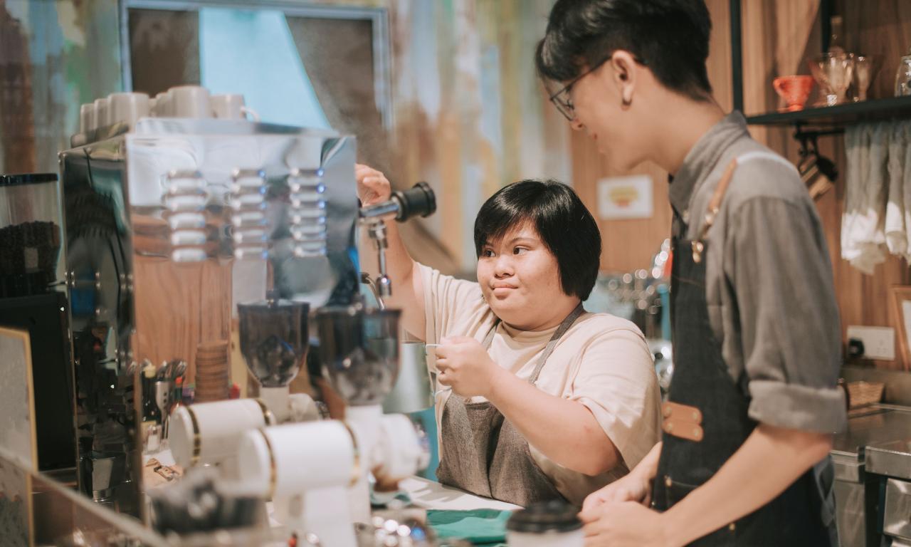 Young man showing young lady how to use drill machine in workshop