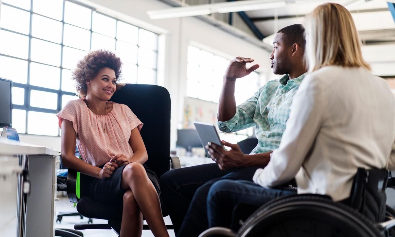 Small group of work colleagues sat down, one in wheelchair, talking together