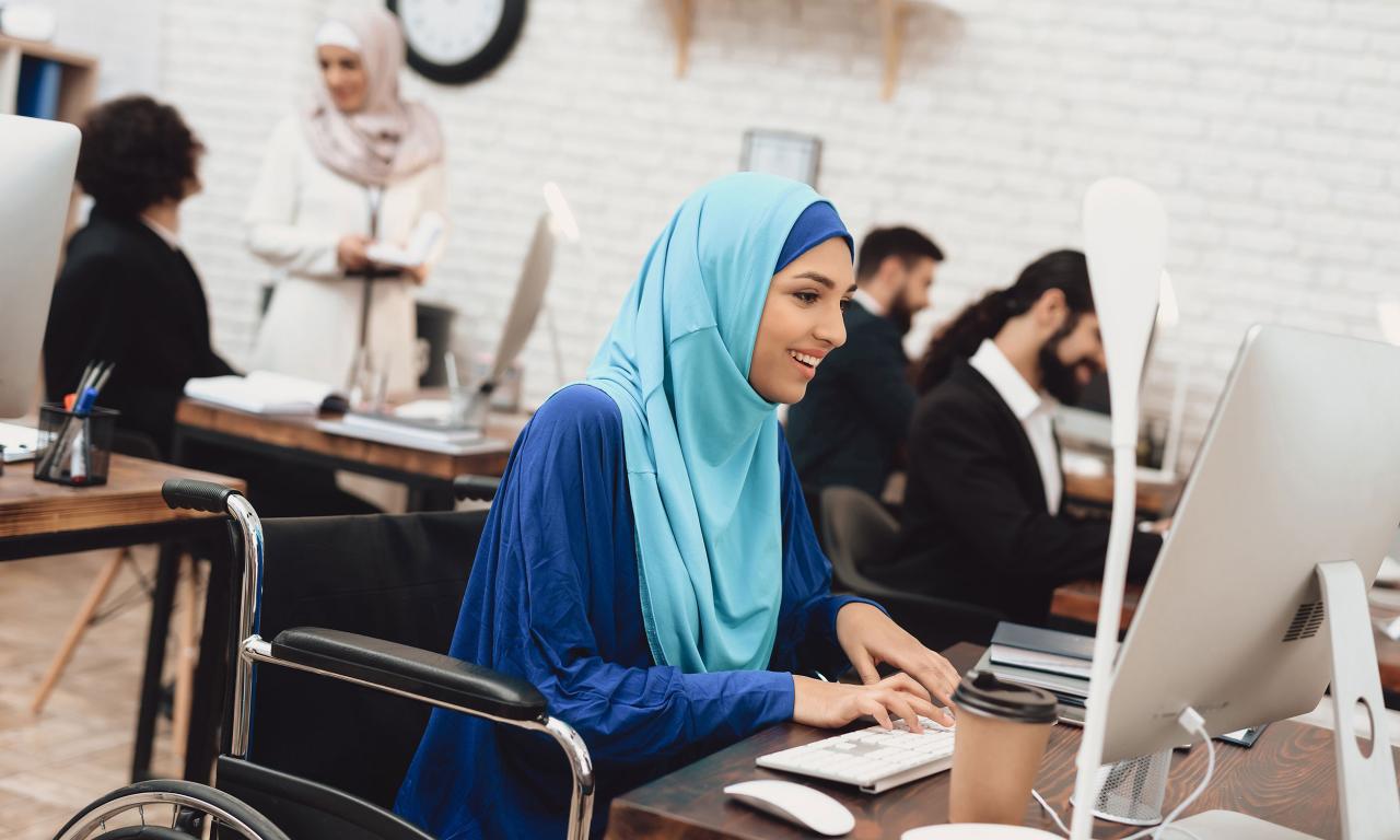 Lady with head scarf and in wheelchair with other co-workers working on computers