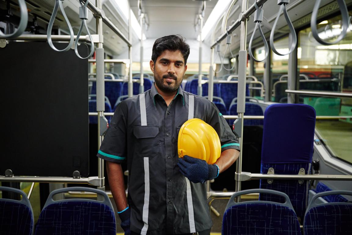 Young Indian man with standing in an empty train holding yellow hard hat in left hand