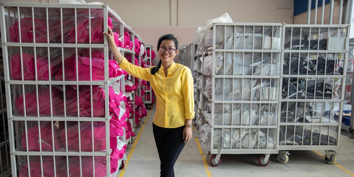 Lady in black trousers and yellow shirt standing in front of tall baskets with laundry bags