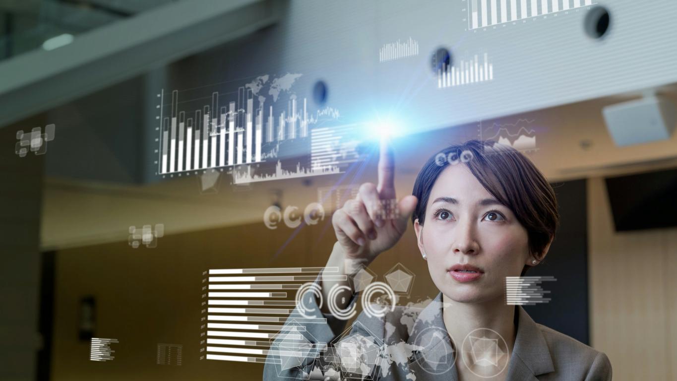 Lady looking and pointing on a digitalized transparent screeen with graphs