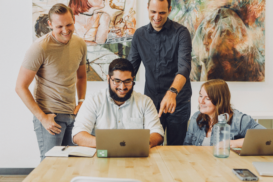 Group of 4 people sitting and standing around a laptop