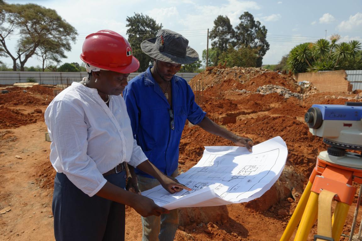 Lady with red hard hat showing plans to worker on construction site in Zambia