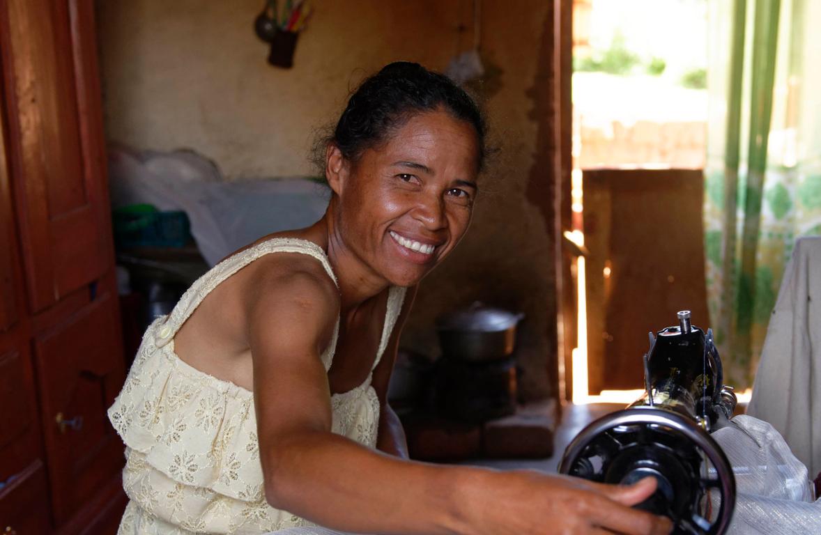 Lady using hand sewing machine in her house smiling