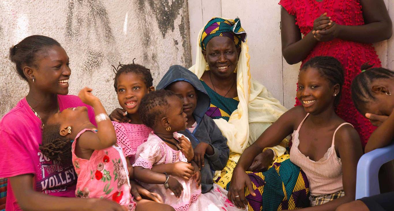 Astou Gningue sits smiling, surrounded affectionately by her family. Pikine, Senegal.