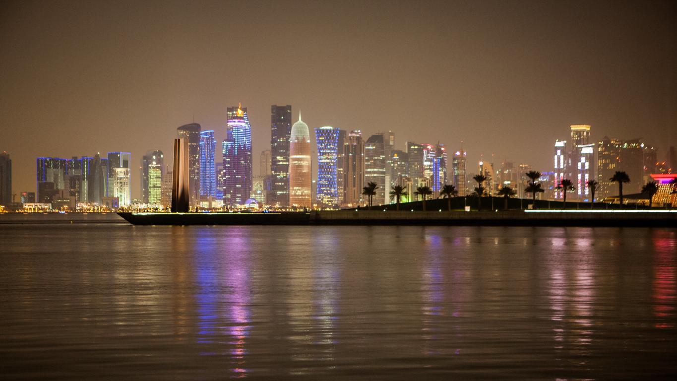 Night time image of tall building with lights in the background with water in foreground