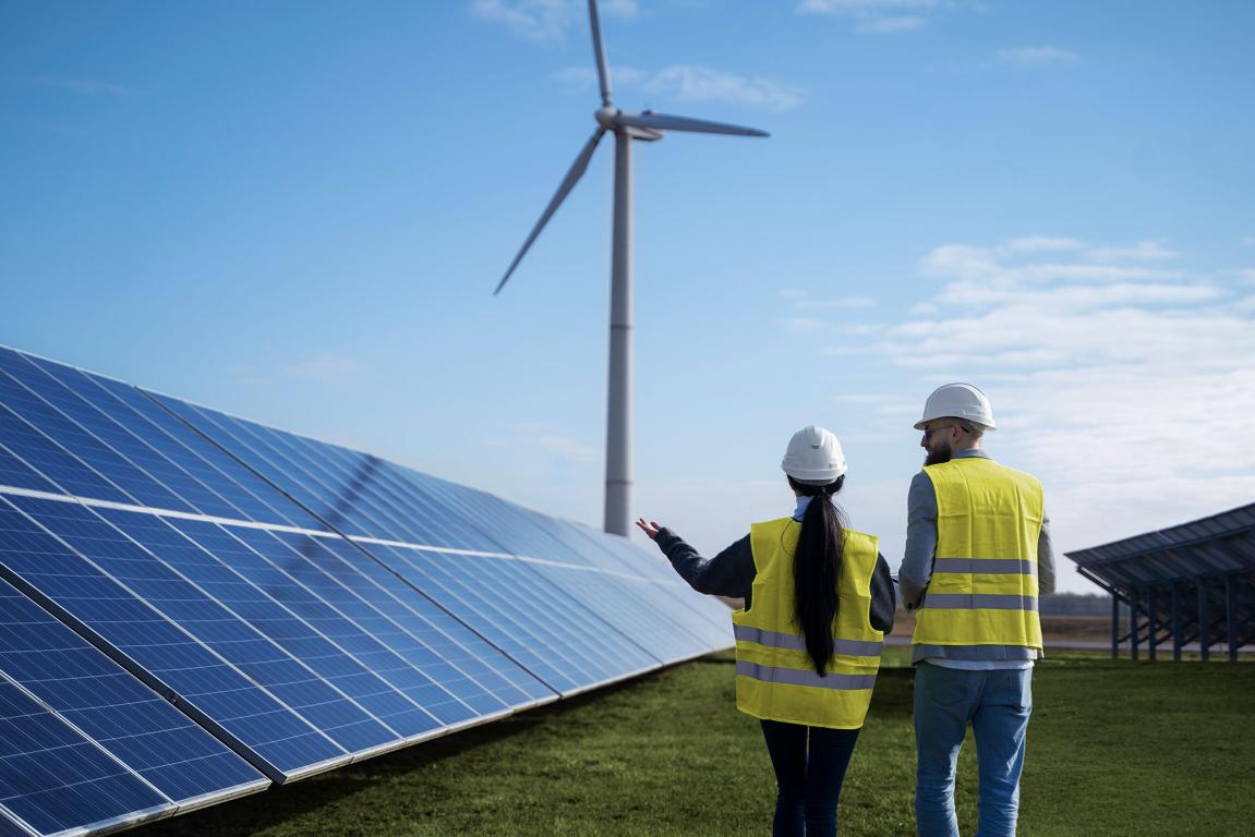 back shot of lady and man in yellow jackets walking past solar panels