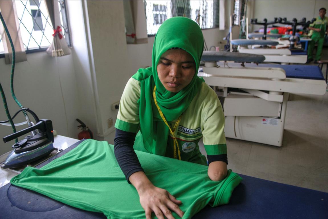 Young Asian lady with a hand malformation wearing a green scarf ironing a green shirt