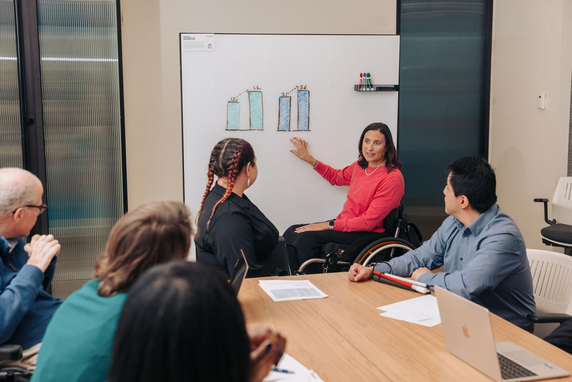 Lady in wheelchair giving a presentation to other colleagues around the table
