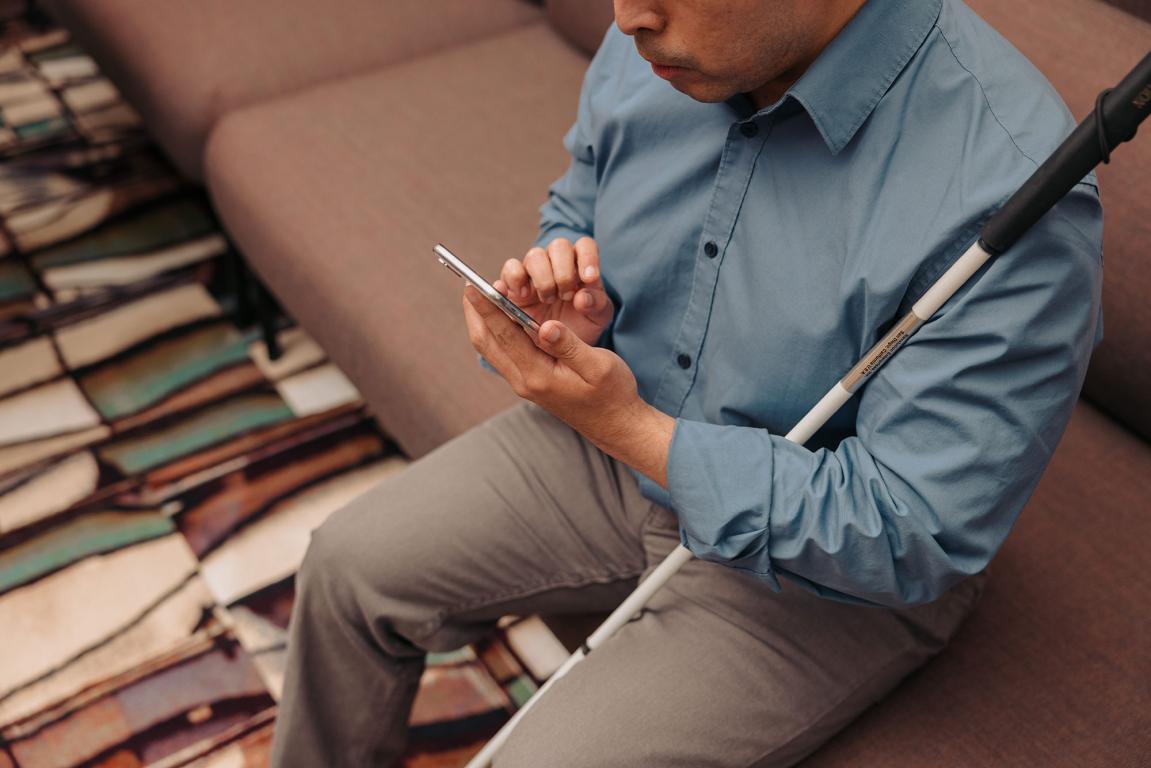 Man with guide stick sat on sofa looking at a telephone