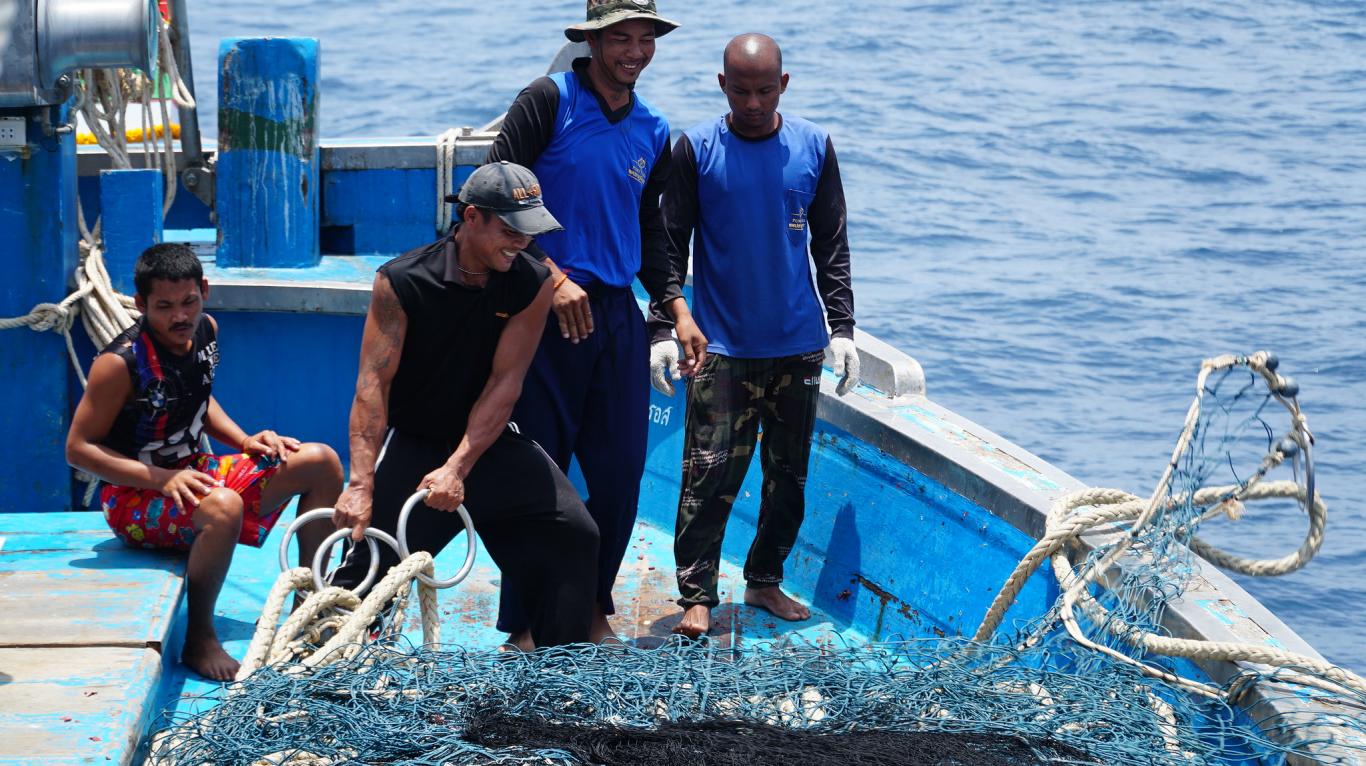 A group of fisherers trowing net from their fishing boat into the sea, smiling