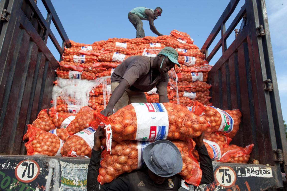 Three black men with hats unloading lorry of large bags of onions