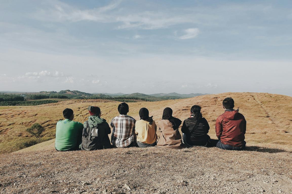 View of peoples' back sitting on hill under cloudy sky