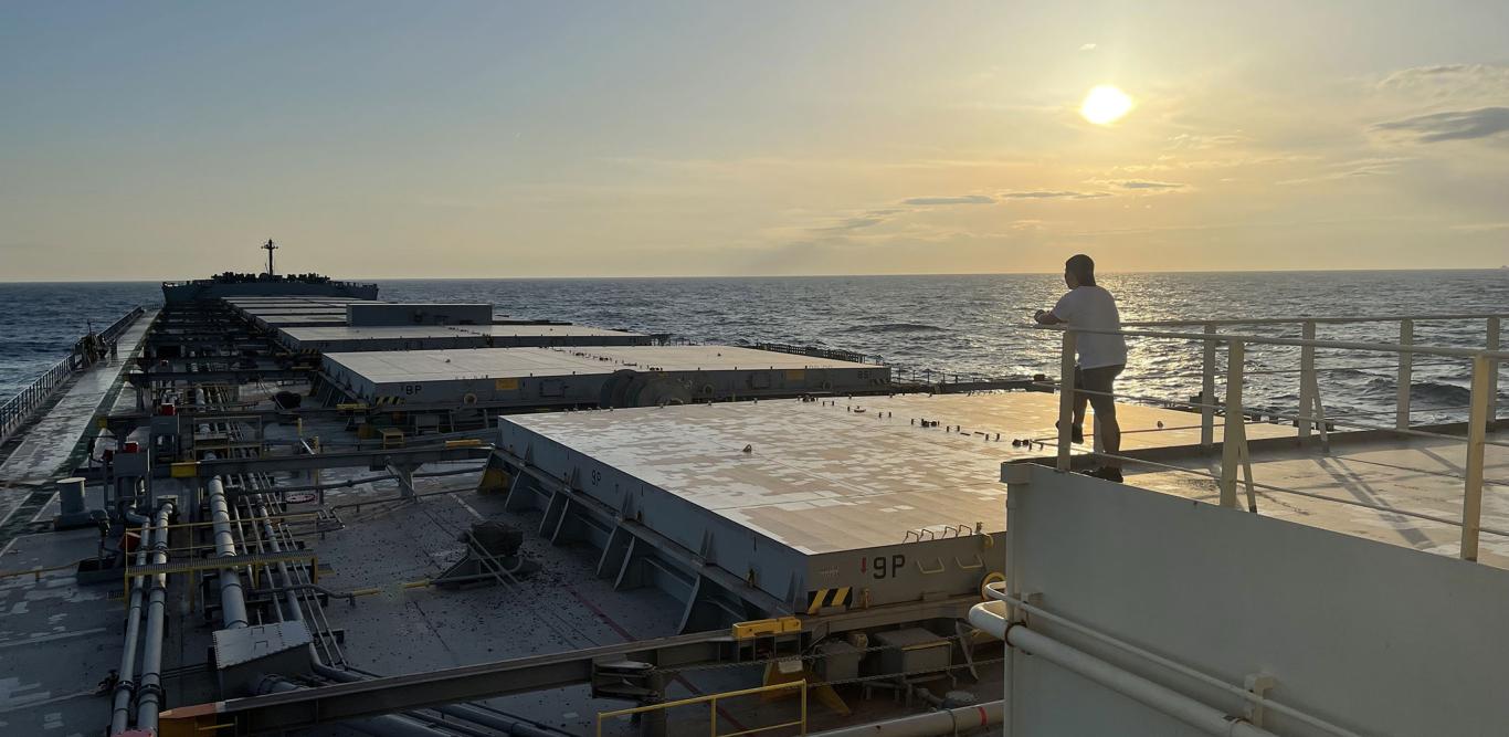 Crew member on the deck of a cargo ship overlooking the ocean at sunset