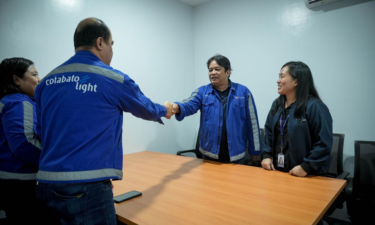 Four people are standing around a table. Two of them are shaking hands.