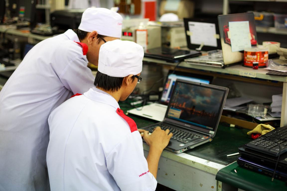 Two technicians in uniforms working on laptops in a laboratory setting