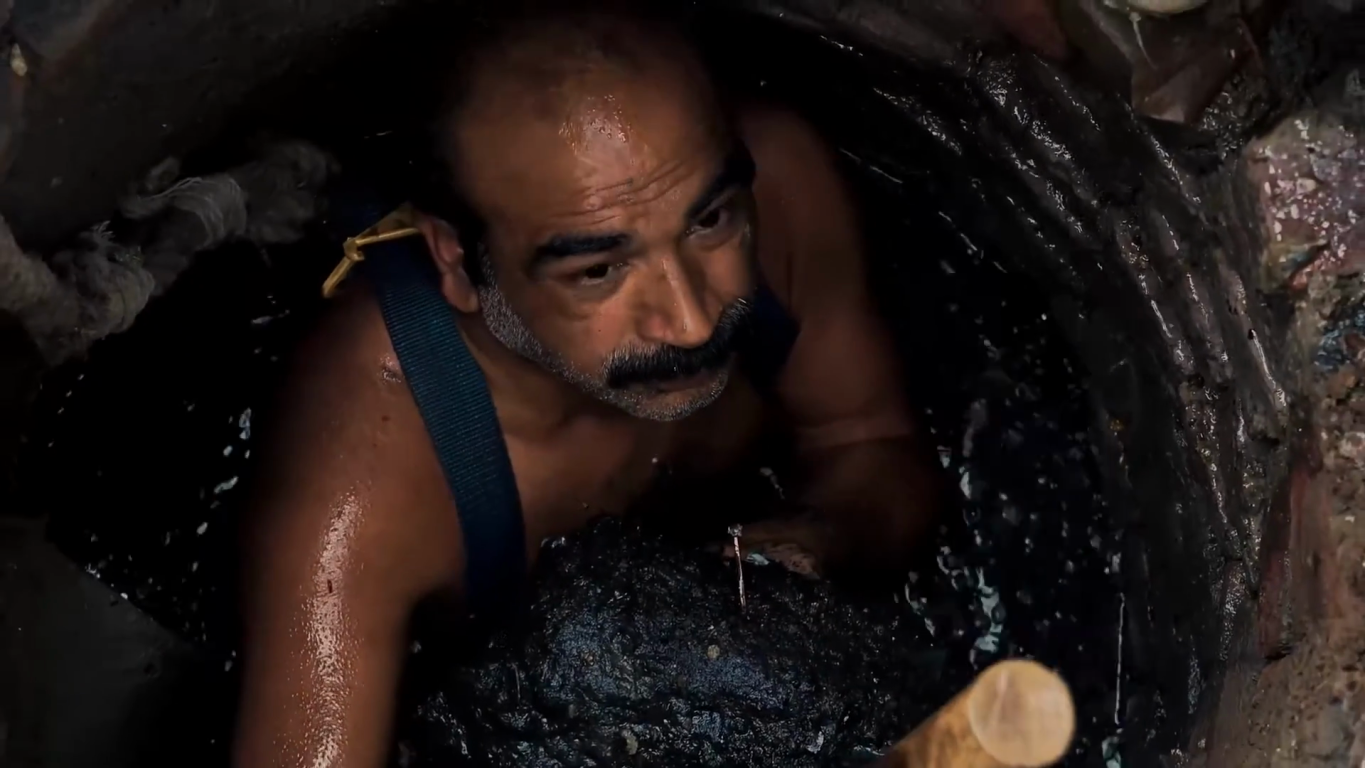 A man emerging sweaty from a manhole