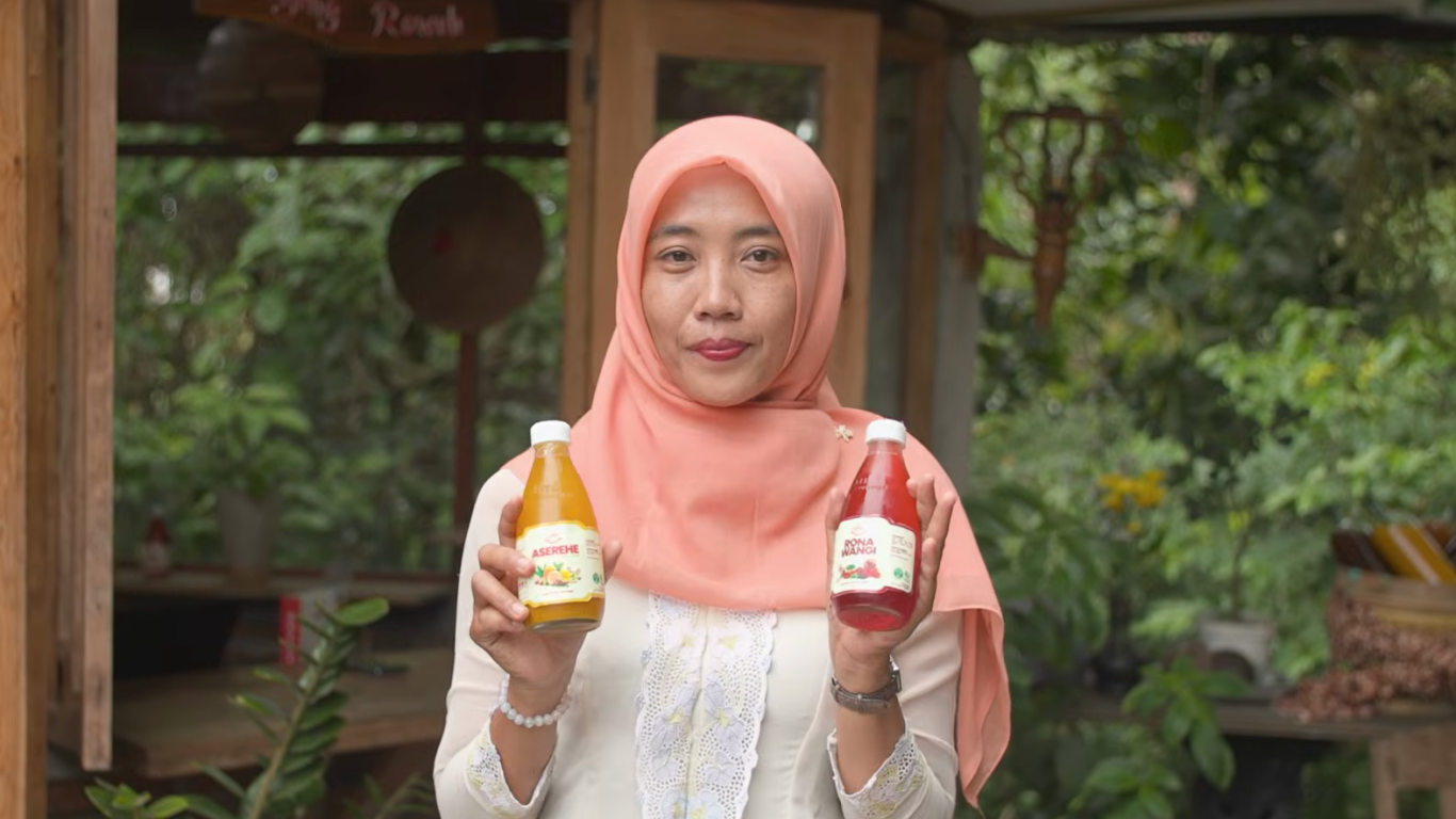 Woman in pink headscarf holds up bottles of juice