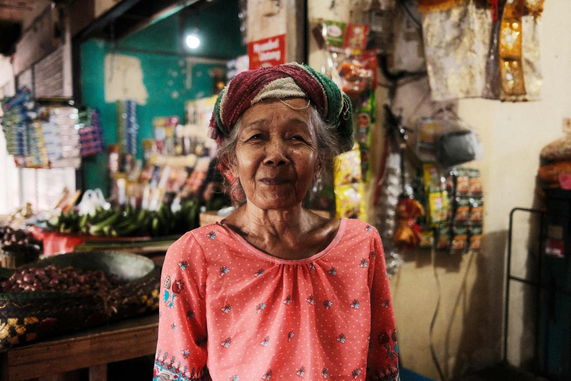 An elderly woman stands in her small shop