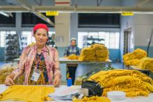 Lady in TShirt factory measuring the width of a shirt with another worker at another work station behind