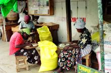 Three African women with headdress on wooden stools sifting through flour
